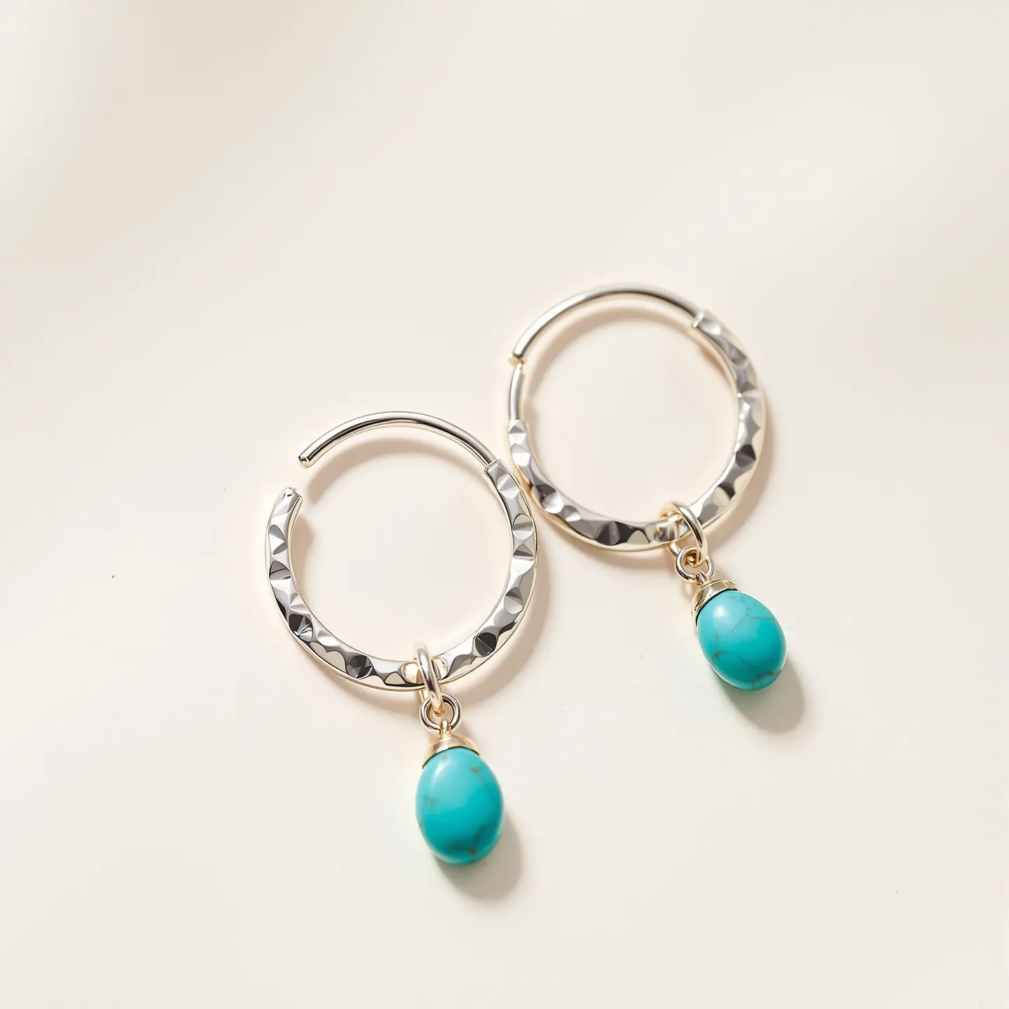A pair of hammered sterling silver hoop earrings with small oval turquoise drops